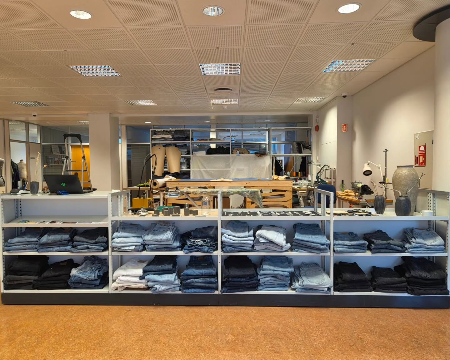Folded denim in front of worktables, tools and equipment in the working creative studio behind the shop.